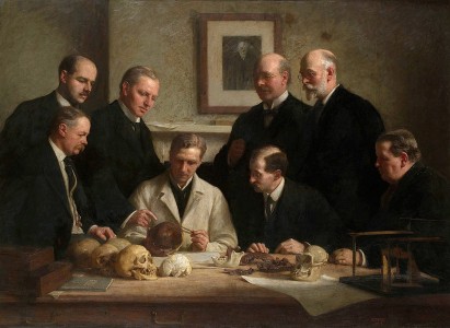 “Discussione attorno al cranio di Piltdown” (John Cooke, 1915, Geological Society of London, UK). Dal centro verso sinistra, in senso orario: A. Keith, anatomista (seduto); A.S. Underwood, chirurgo dentale-anatomista; F.O. Barlow, tecnico dei calchi; G.E. Smith, anatomista; C. Dawson, amateur; A. Smith Woodward, paleontologo; E.R. Lankester, zoologo; W.P. Pycraft, zoologo (seduto). Sul muro di fondo, un ritratto di C.R. Darwin (immagine web: blog.geolsoc.org.uk/2012/12/13/a-tale-of-three-meetings/geological/)